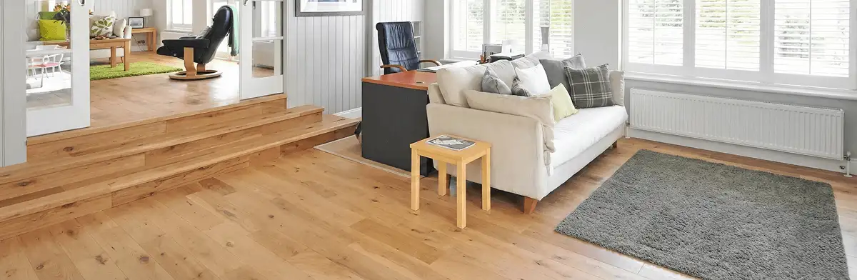 A modern living room with professionally installed laminate flooring, a beige sofa, a small side table, a gray rug, and large windows with white shutters in Hollywood, FL
